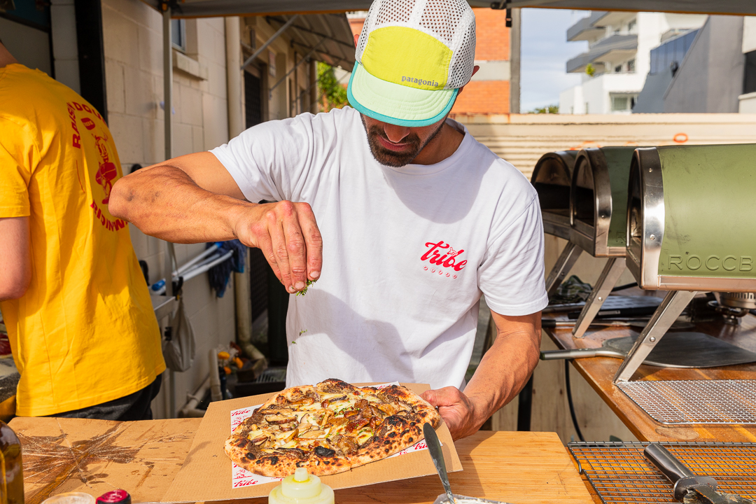 Tribe chef sprinkling herbs over a freshly baked sourdough pizza